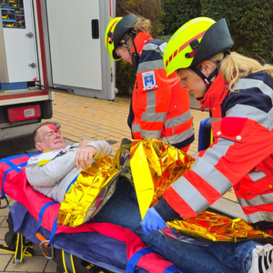 Zwei Auszubildende des Rettungsdienstes mit einer verletzten Person auf der Trage bei einer Übung.
